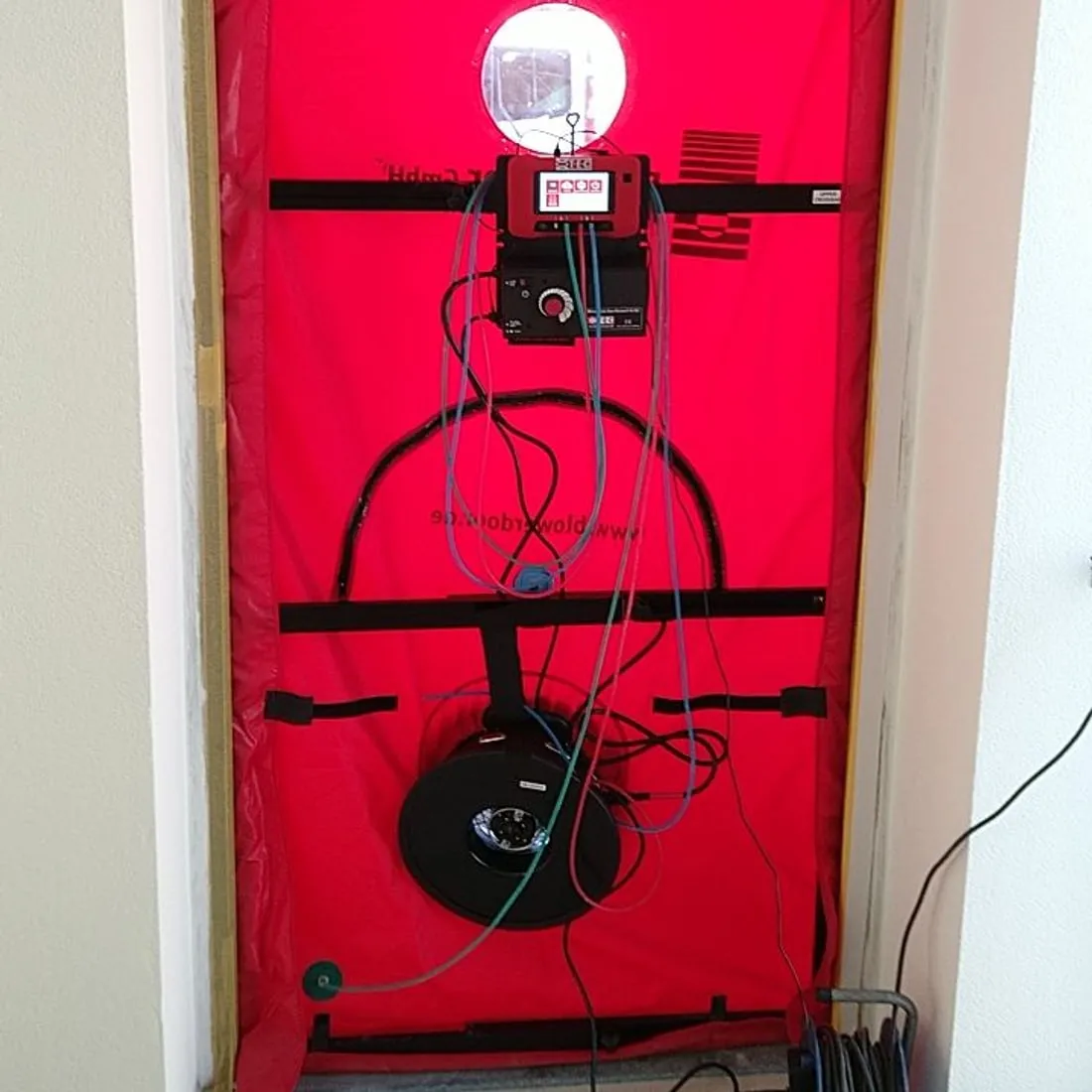 BlowerDoor-Messung: Ventilator und Messgerät in einer roten Einbauplane in der Haustür